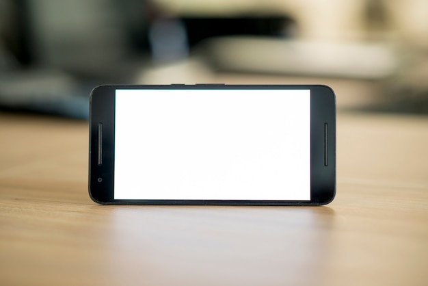 Smartphone com tela branca em branco sobre a mesa de madeira