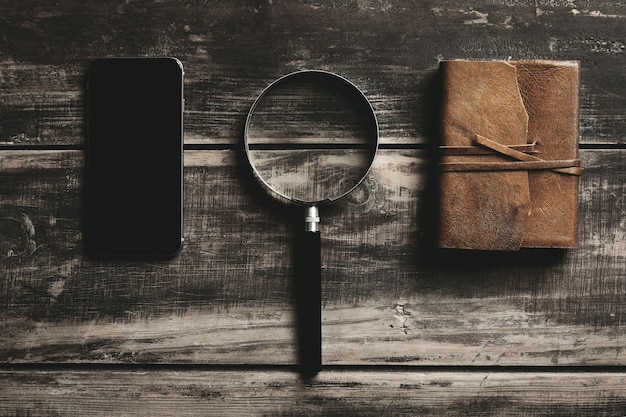 Smartphone móvel, lupa e notebook com capa de couro isolado na mesa de madeira preta da fazenda