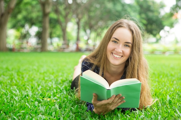 Smiling Beautiful Girl Deitada na grama com o livro