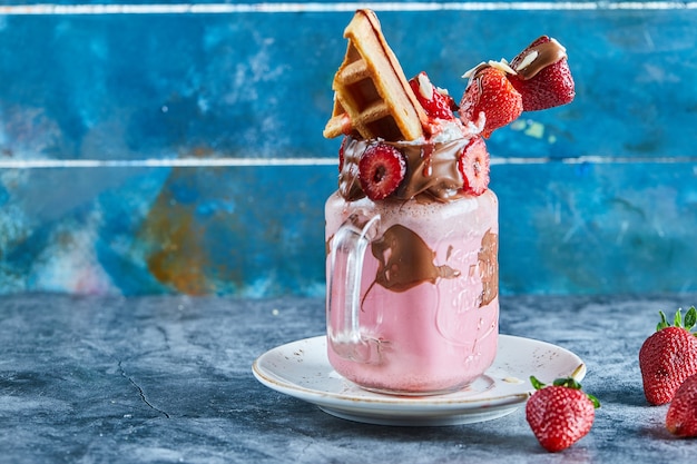 Smoothie de morango com waffle minúsculo, chocolate e fatias de morangos no prato branco na superfície azul escura