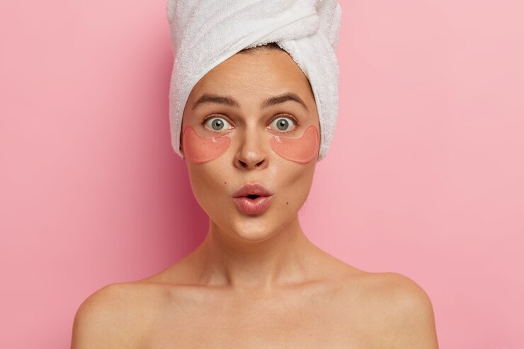 Foto grátis sob o conceito de tratamento de olhos e cuidados com o corpo. mulher caucasiana chocada aplica adesivos de beleza, remove olheiras e inchaços, olha-se surpreendentemente no espelho, fica de topless em casa