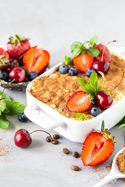 Foto grátis sobremesa italiana clássica tiramisu decorada com morangos, cerejas e hortelã sobre fundo branco