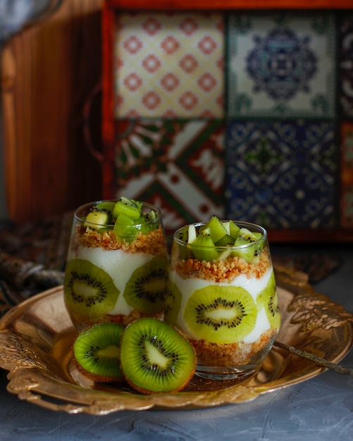 Sobremesa saudável de iogurte com granola e kiwi fresco cortado em copos altos.