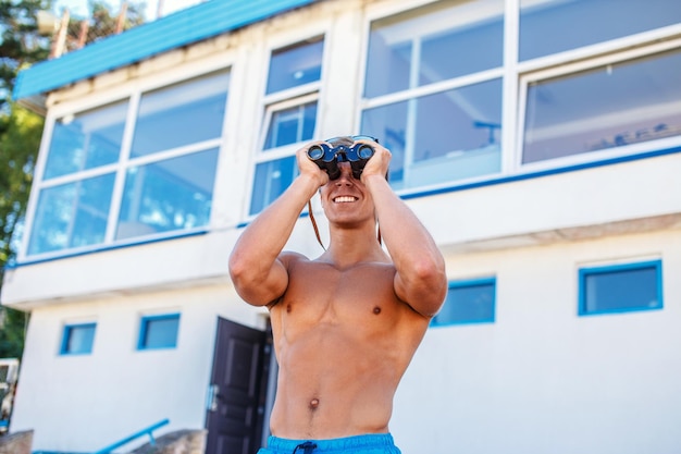 Foto grátis socorrista de mar muscular sem camisa olhando no binóculo.