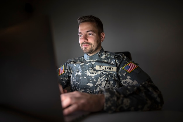 Soldado americano em uniforme militar com sinalizadores de patch dos eua trabalhando até tarde no computador