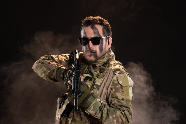 Soldado camuflado segurando uma metralhadora em uma parede escura