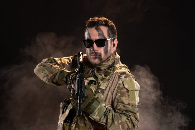 Soldado camuflado segurando uma metralhadora em uma parede escura