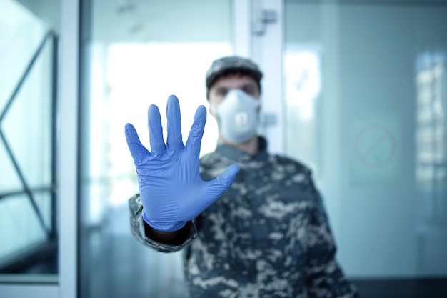 Soldado em uniforme de camuflagem militar em frente à entrada do hospital e mostrando sinal de pare