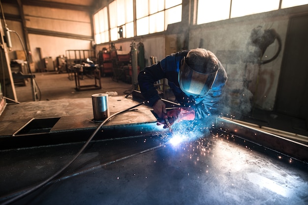 Soldador profissional soldando peças de construção de metal em oficina industrial