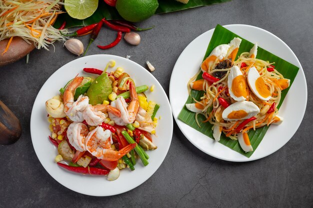 Som Tum com Milho e Camarão, servido com macarrão de arroz e salada verde. Decorado com ingredientes da comida tailandesa.