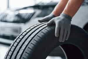 Foto grátis somente mãos. mecânico segurando um pneu na oficina. substituição de pneus de inverno e verão