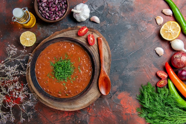 Sopa clássica de tomate em uma tigela marrom, garrafa de óleo, grãos e colher na mesa de cores diferentes