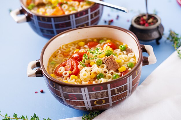 Sopa com macarrão pequeno, legumes e pedaços de carne na tigela na mesa azul. Comida italiana.