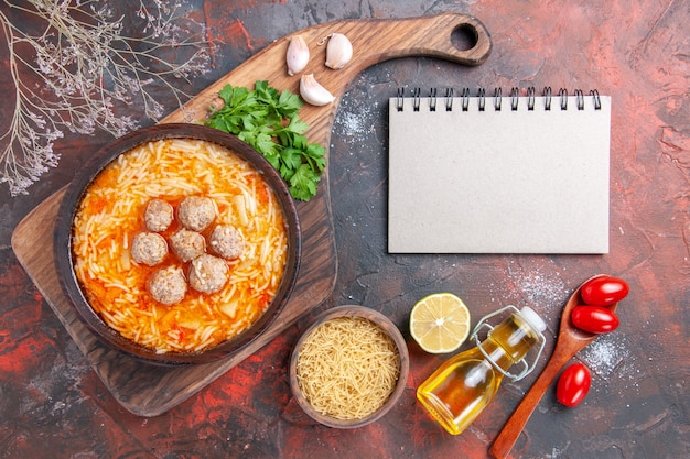 Sopa de almôndegas com macarrão a bordo de massas crus, folhas de limão e caderno em fundo escuro.