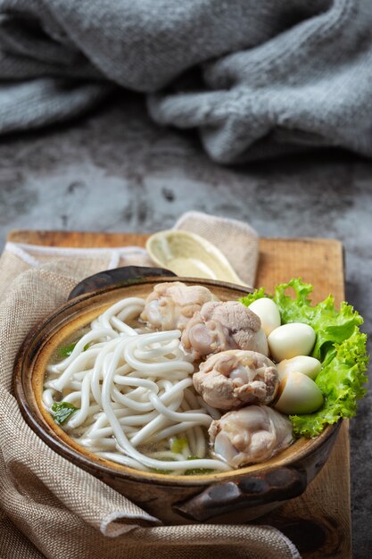 Sopa de estilo asiático com macarrão, carne de porco e cebolinha estreitamente em uma tigela em cima da mesa.