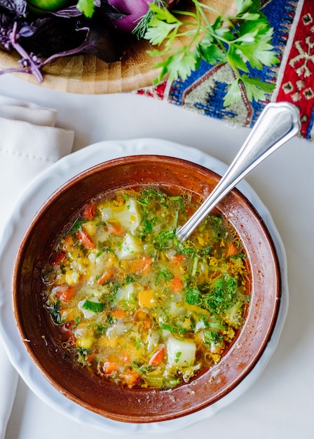 Sopa de legumes com ervas dentro da tigela marrom.