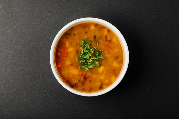 Sopa de lentilha com ingredientes misturados e ervas em uma tigela branca.