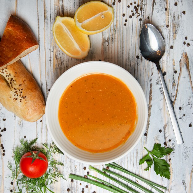 Sopa de lentilha vermelha com limão, tomate, pão, ervas, especiarias, colher em uma tigela