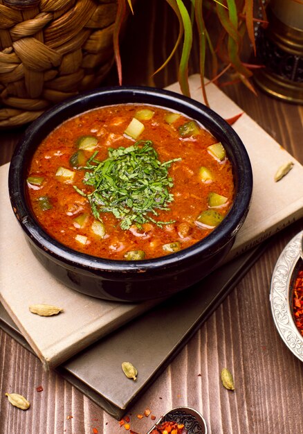 Sopa de tomate abobrinha com ervas na tigela preta sobre os livros