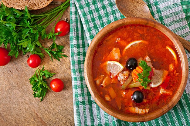 Sopa solyanka russo com carne, azeitonas e pepinos em uma tigela de madeira