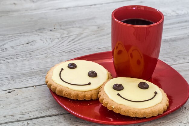 sorria biscoitos num prato vermelho com uma xícara de café, fundo de madeira, comida