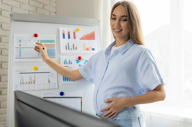 Sorridente empresária grávida fazendo apresentação no quadro branco