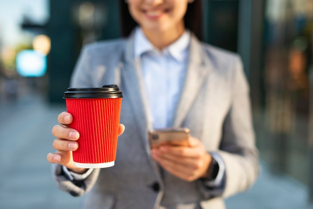Sorridente empresária usando smartphone enquanto toma café