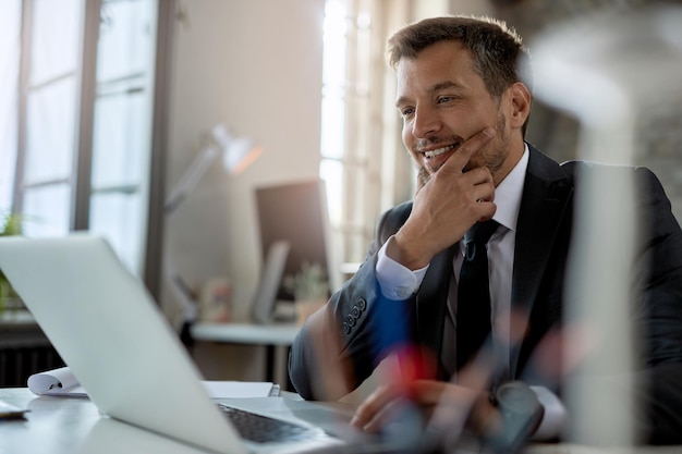 Sorridente empresário adulto médio usando computador enquanto trabalhava na mesa de escritório