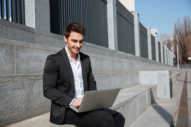 Sorridente jovem empresário sentado ao ar livre.