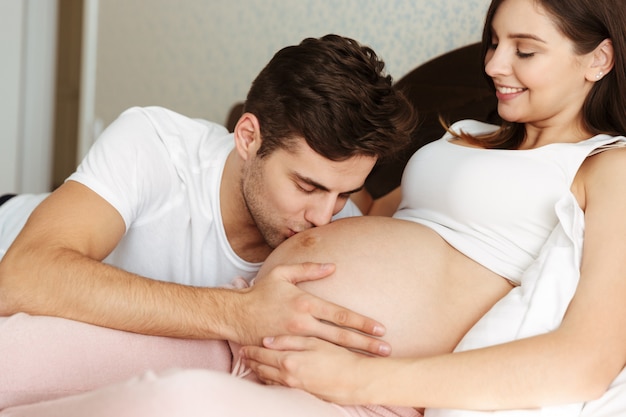 Sorridente jovem esposa grávida deitada na cama