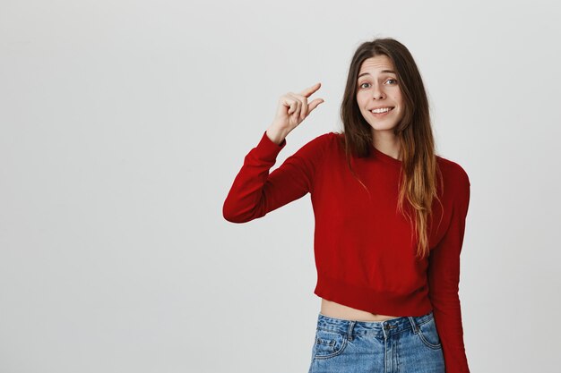 Sorridente menina cute mostrando algo pequeno, minúsculo ou pequeno com gesto com a mão