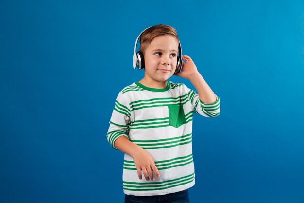 Sorridente menino ouvindo música pelo fone de ouvido e olhando de lado