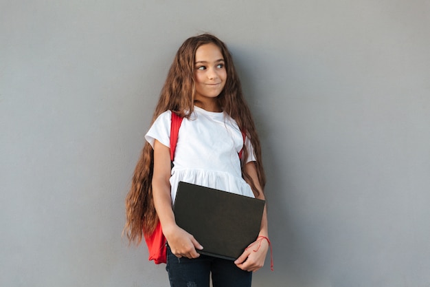 Sorridente mistério morena colegial com cabelo comprido, abraçando o livro