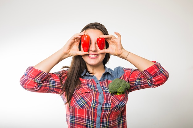Sorridente mulher segurando pimentas perto dos olhos