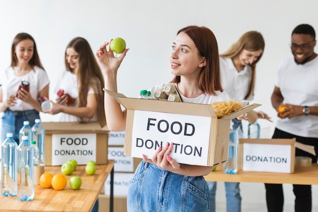 Sorridente voluntária segurando uma caixa de doação de alimentos com uma maçã