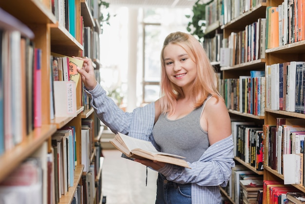 Sorrindo, adolescente, levando, livro, de, estante