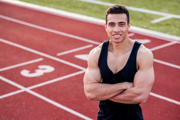 Foto grátis sorrindo atleta bonito com uma roupa desportiva com os braços cruzados na pista de corrida, olhando para a câmera