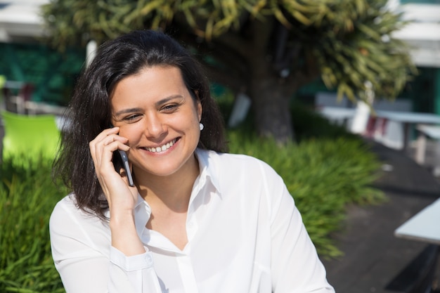 Sorrindo, atraente, mulher fala telefone móvel, ao ar livre