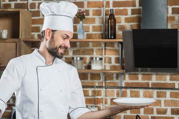 Sorrindo chef segurando um prato branco vazio na mão