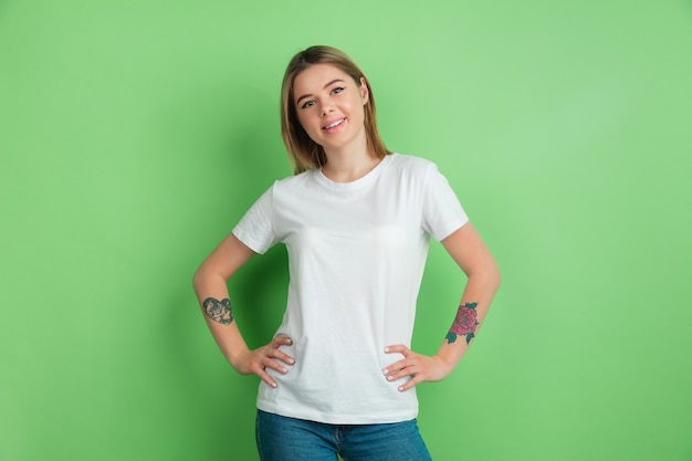 Foto grátis sorrindo, confiante. retrato de uma jovem branca na parede verde do estúdio