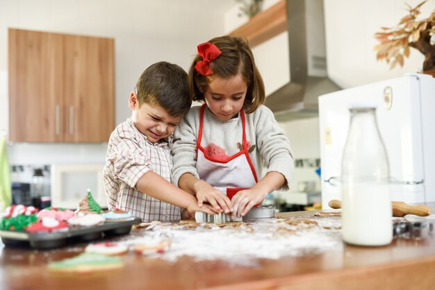 Sorrindo crianças que decoram bolinhos do Natal na cozinha