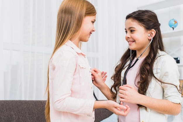 Sorrindo, duas meninas, desfrutando, jogando doutor, e, hospitalar, usando, estetoscópio, casa