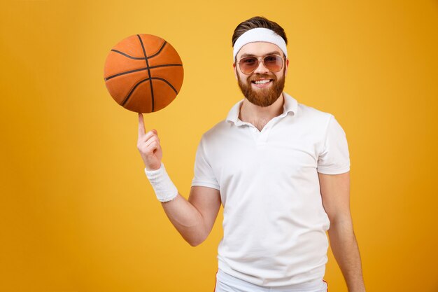 Sorrindo esportista em óculos de sol segurando basquete no dedo