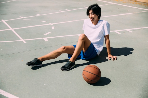 Sorrindo esportiva jovem sentado na quadra de basquete