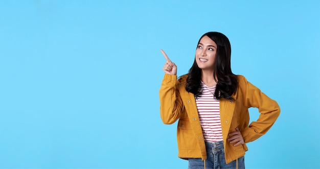 Sorrindo feliz mulher asiática com seu dedo apontando isolado na luz - fundo azul bandeira com espaço de cópia.