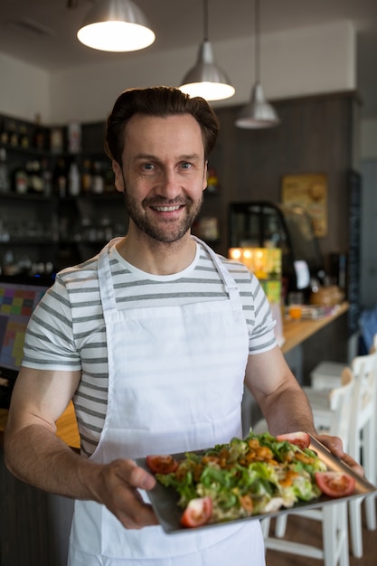 Sorrindo garçom carregando uma bandeja de salada no restaurante