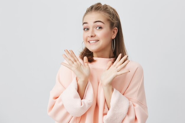 Sorrindo garota de cabelos claros com os braços abertos, encolhendo os ombros, executando e dizendo: Eu não sei. Expressões faciais, percepção e atitude da vida