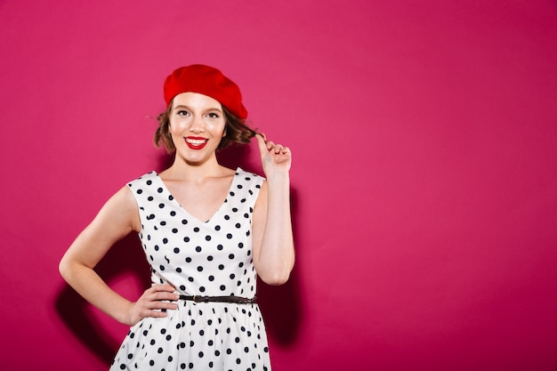 Sorrindo gengibre mulher de vestido com o braço no quadril, olhando para a câmera sobre rosa