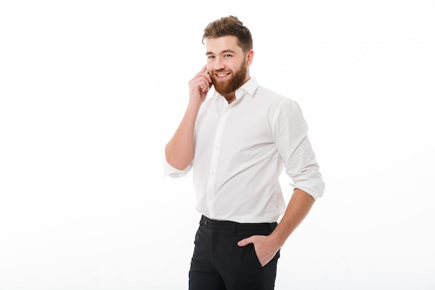 Sorrindo homem barbudo em roupas de negócios falando pelo smartphone