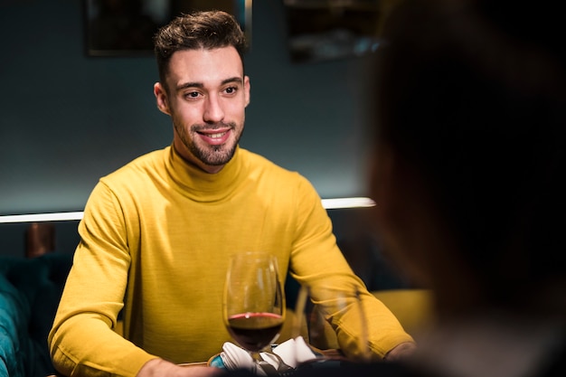 Sorrindo homem e pessoa sentada à mesa com copos de vinho